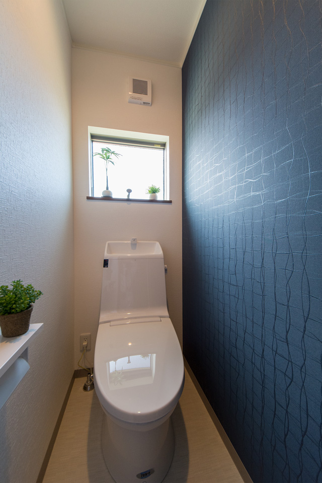 白を基調とした清潔感のある2階トイレ。紺色のアクセントクロスがシックで落ち着きのある空間を演出。