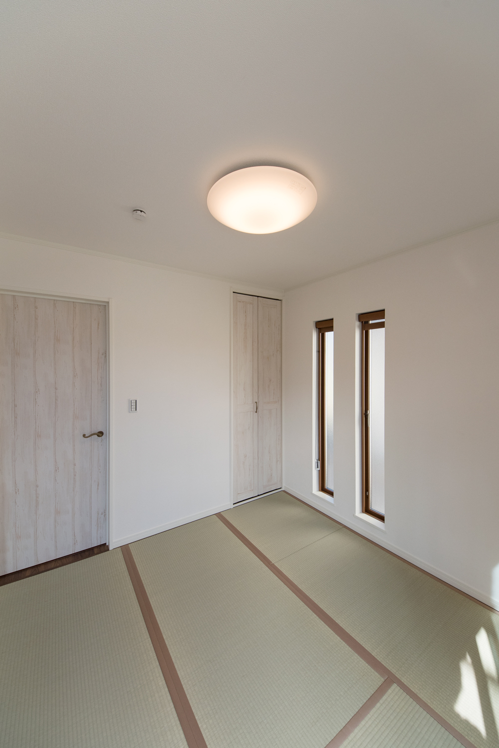 縦長の窓とエイジング加工された白い建具を施した畳敷き洋室。