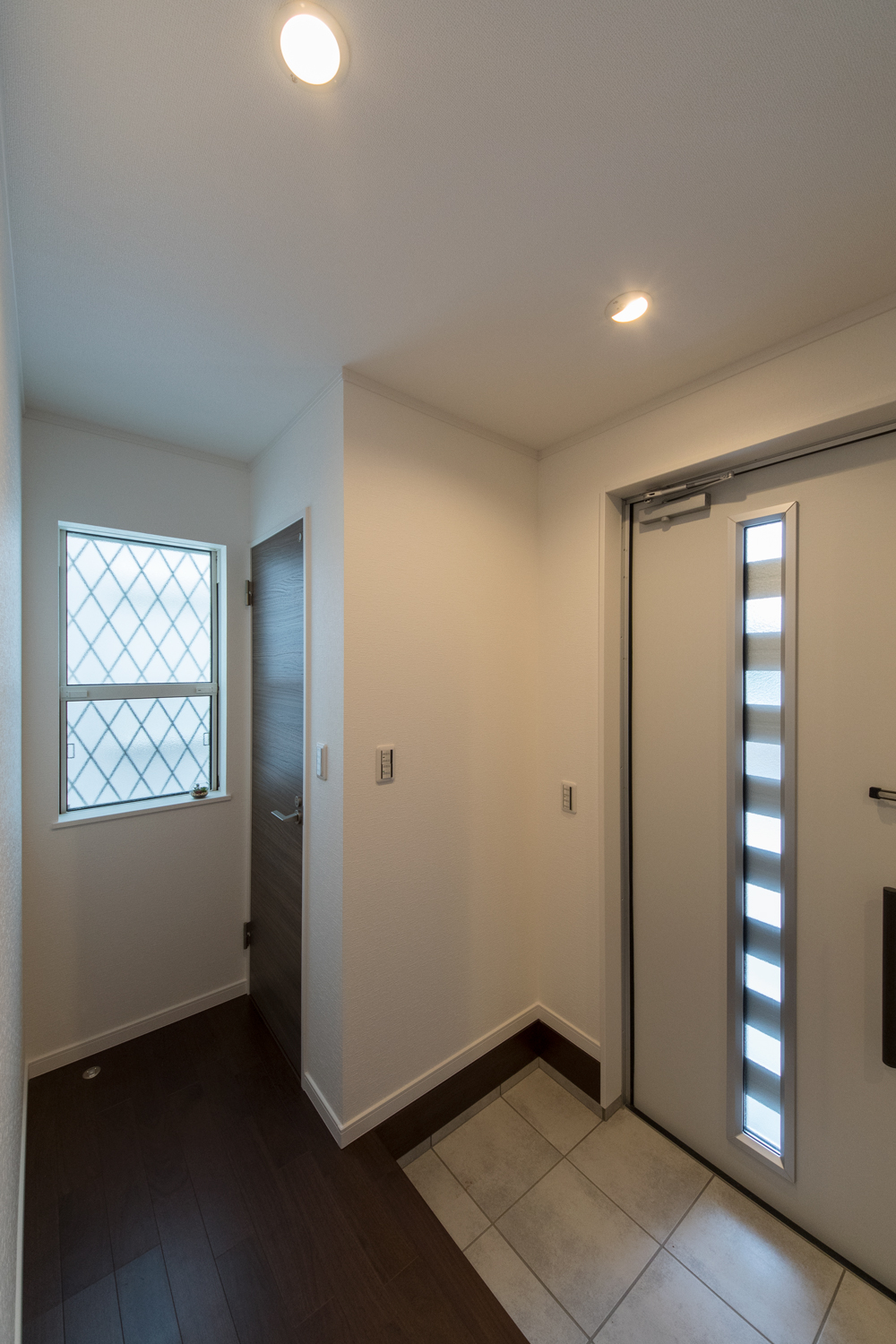 ホワイト×ブラウンのナチュラルな配色の玄関。ドアの窓から自然の光が差し込みます。