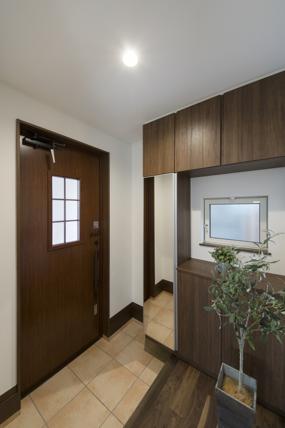 木の温もり感じる木目調のドアと収納、ベージュのテラコッタ調タイルが玄関をナチュラルな雰囲気に包みます。