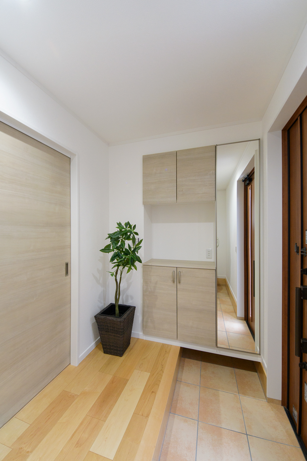 木の温もり感じる玄関ドアと収納、ベージュのテラコッタ調タイルが穏やかな空間を演出。