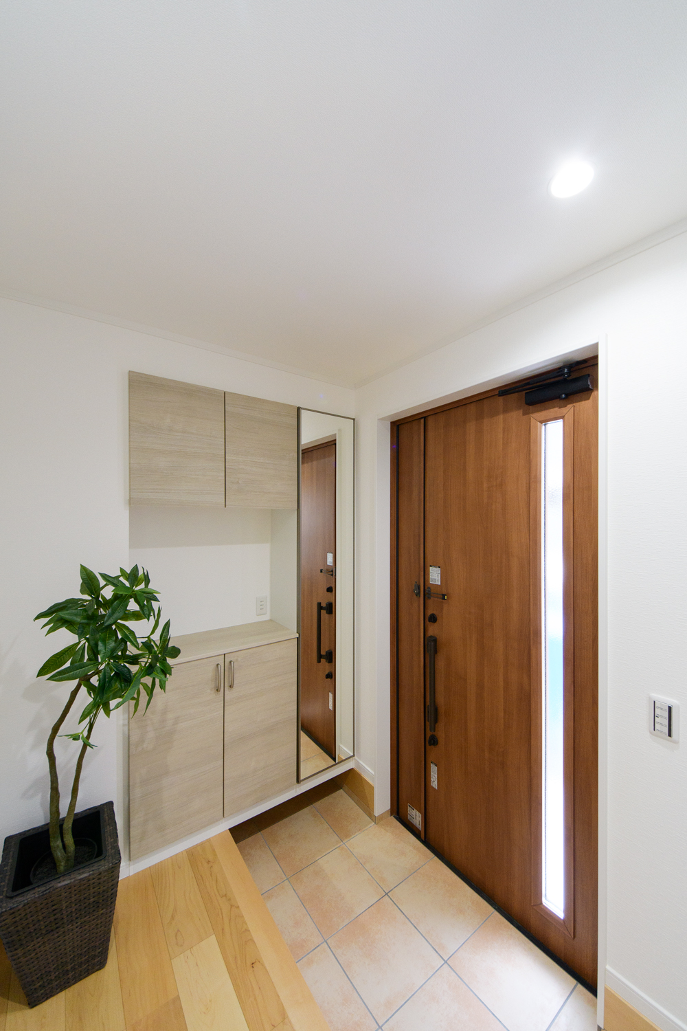 木の温もり感じる玄関ドアと収納、ベージュのテラコッタ調タイルが穏やかな空間を演出。