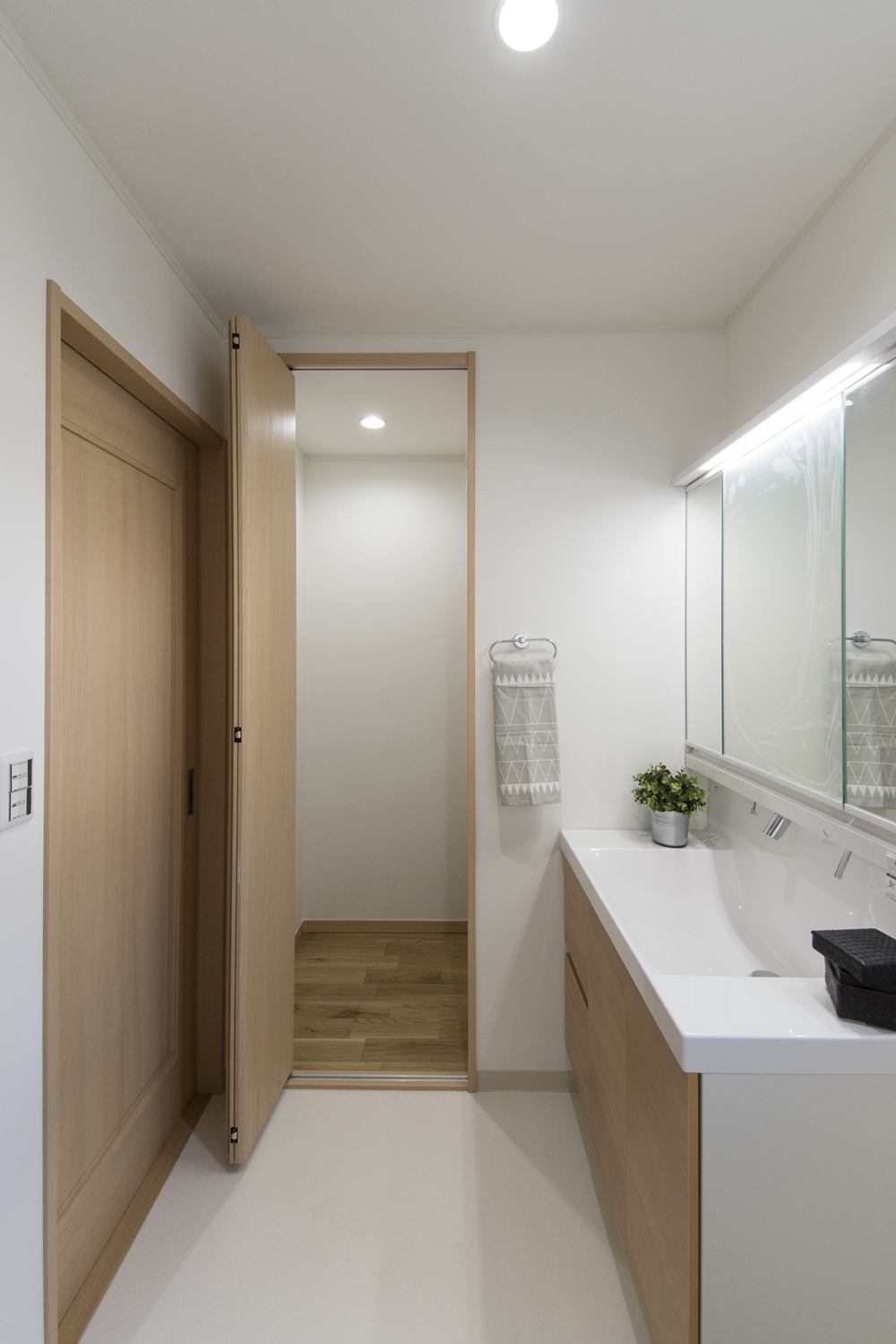 白を基調とした清潔感のあるサニタリールーム。洗面化粧台扉を明るい木目調カラーでアクセント。