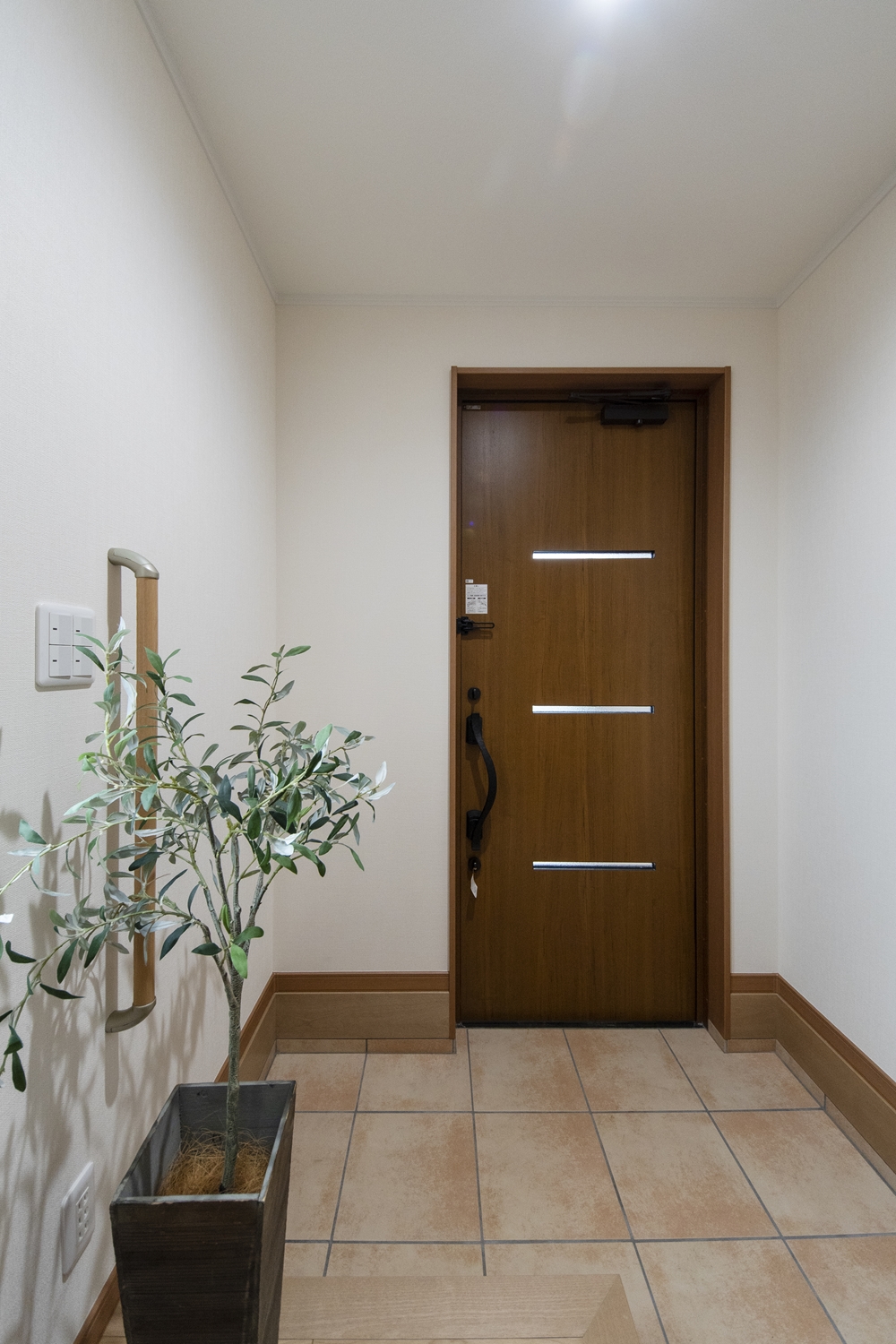 玄関／木目調の玄関扉とベージュのテラコッタ調タイルがナチュラルな雰囲気を演出。